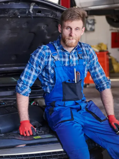 Auto mechanic in overalls sitting at his garage